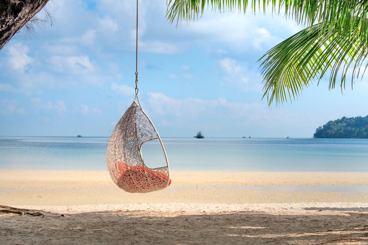 Wicker hanging egg chair on the sand outside a beachfront bungalow